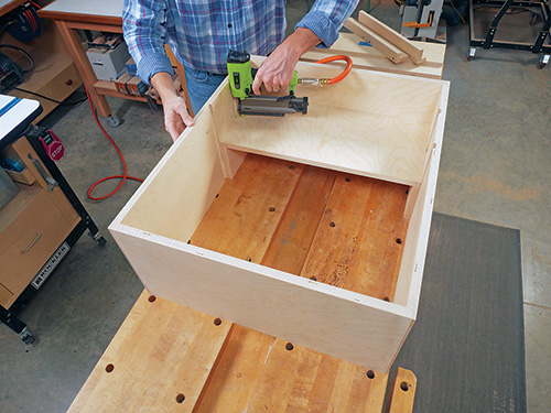 Nailing lower panel in place on tool cabinet