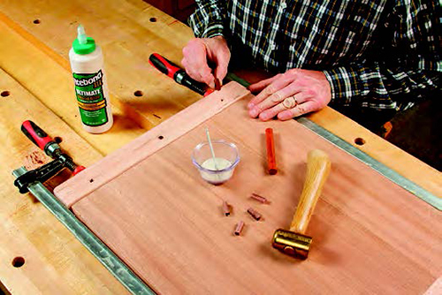 Square pins driven into the breadboard ends and through the panel tenons fasten the parts together. The outer pegs fit into slotted tenon holes.