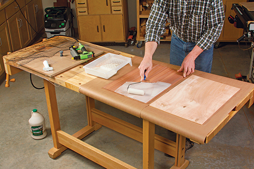 Roll wood glue onto the side panel veneer and its substrate, then assemble the lamination and tack near one edge to keep the panels aligned.