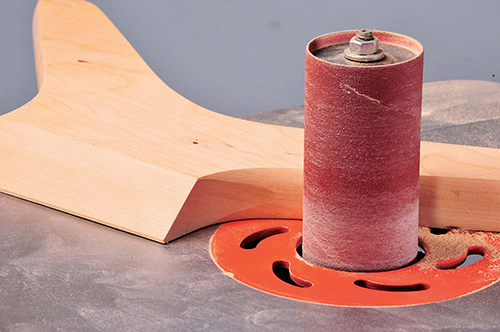 With an oscillating spindle sander, the author sands the leg's fingernail profile flat where the curved leg portion meets the angled straight side.