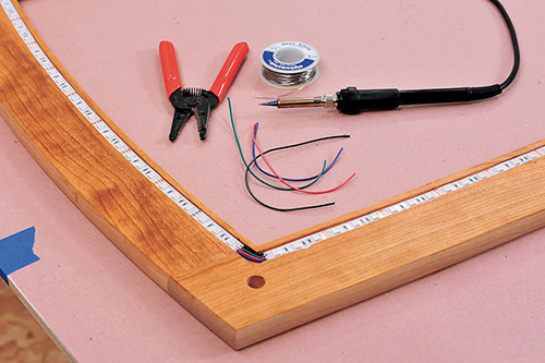 The PSA-backed LED light strip is pressed into a channel routed on the underside of the glass frame and wired together with solder at the corners.