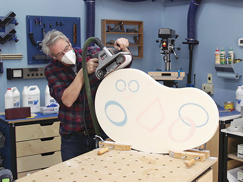 Sanding down sides of kidney table with belt sander