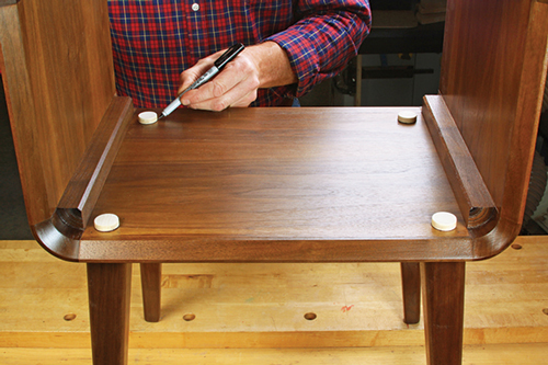 Install the legs on the carcass “dry.” Then mark the protruding tenons for a flush fit with the bottom panel. Trim off this excess at the miter saw with your V-groove jig.