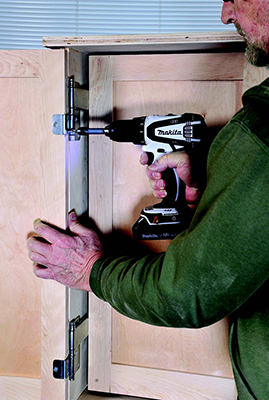 The author drives screws to attach the tandem hinges that mount two pairs of doors to the upper tool cabinet. The 2" space between each pair of doors provides room for hanging small tools and supplies.