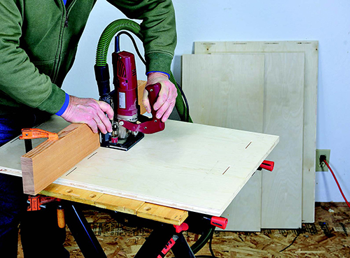 To cut matching slots in panel faces, the author clamped a straight board to the panel as a fence. With the base of his joiner against this fence, he plunged the blade down to cut slots.