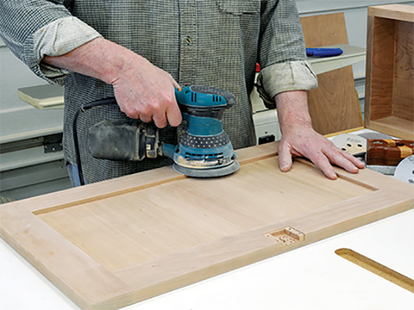 Using a hand sander to smooth parts for a door panel