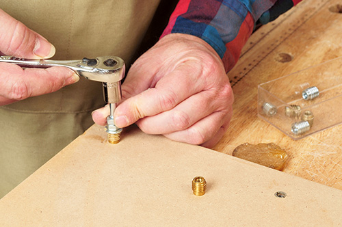 Using a socket wrench to attach a bolt to router table base