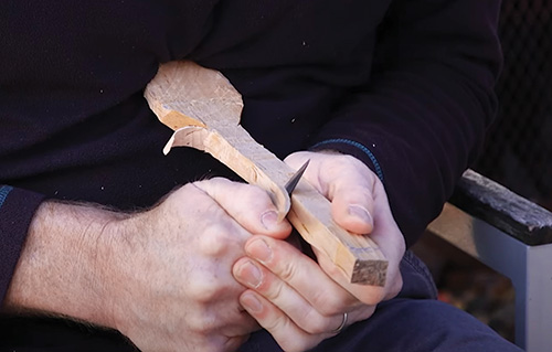 Pulling carving cut with spoon blank braced against chest