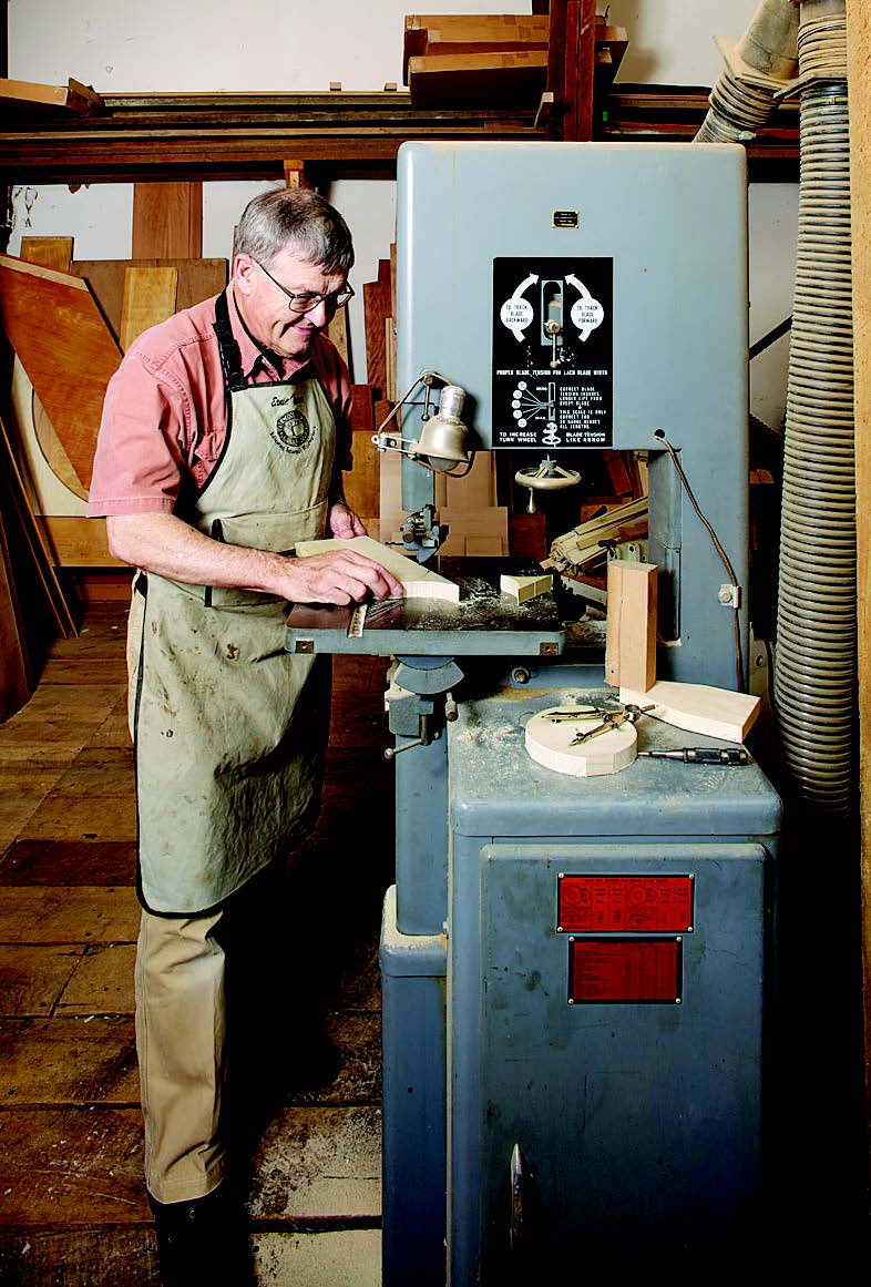 The author uses a drill press to drill to the axle diameter he has laid out for wooden wheels. Band saw just outside the layout lines.