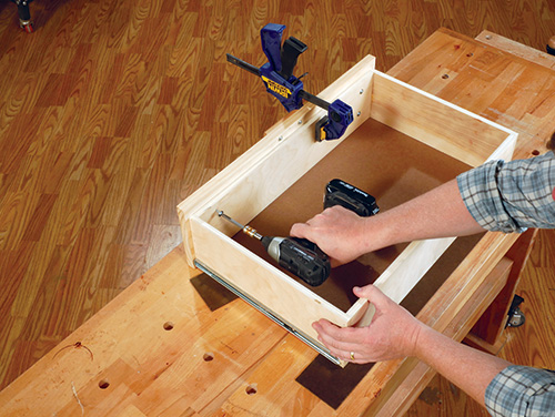 Screwing drawer face in place on wall cabinet drawers